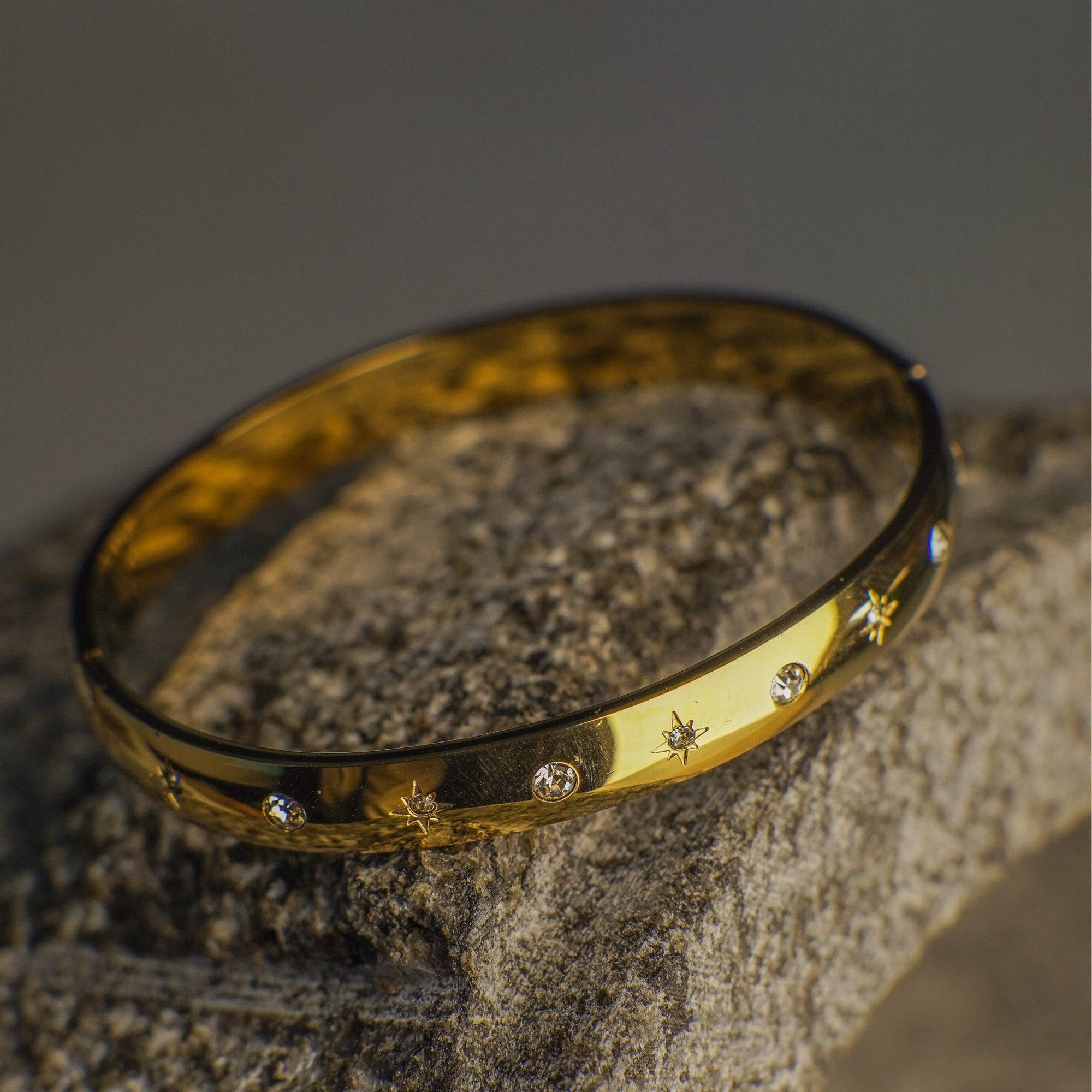 Gold bracelet with star and diamond designs on a textured stone surface