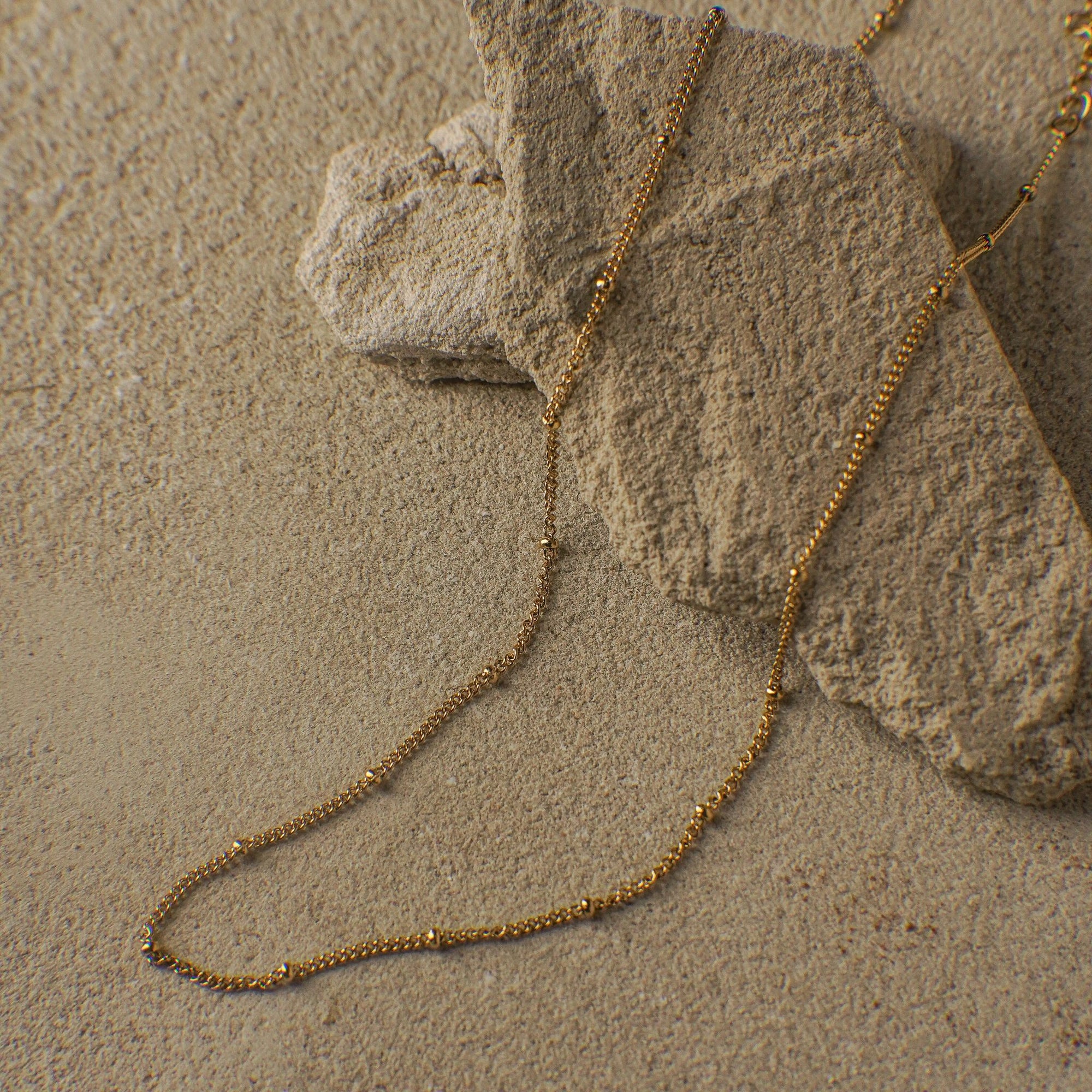 Gold chain necklace on a sandy surface with rocks