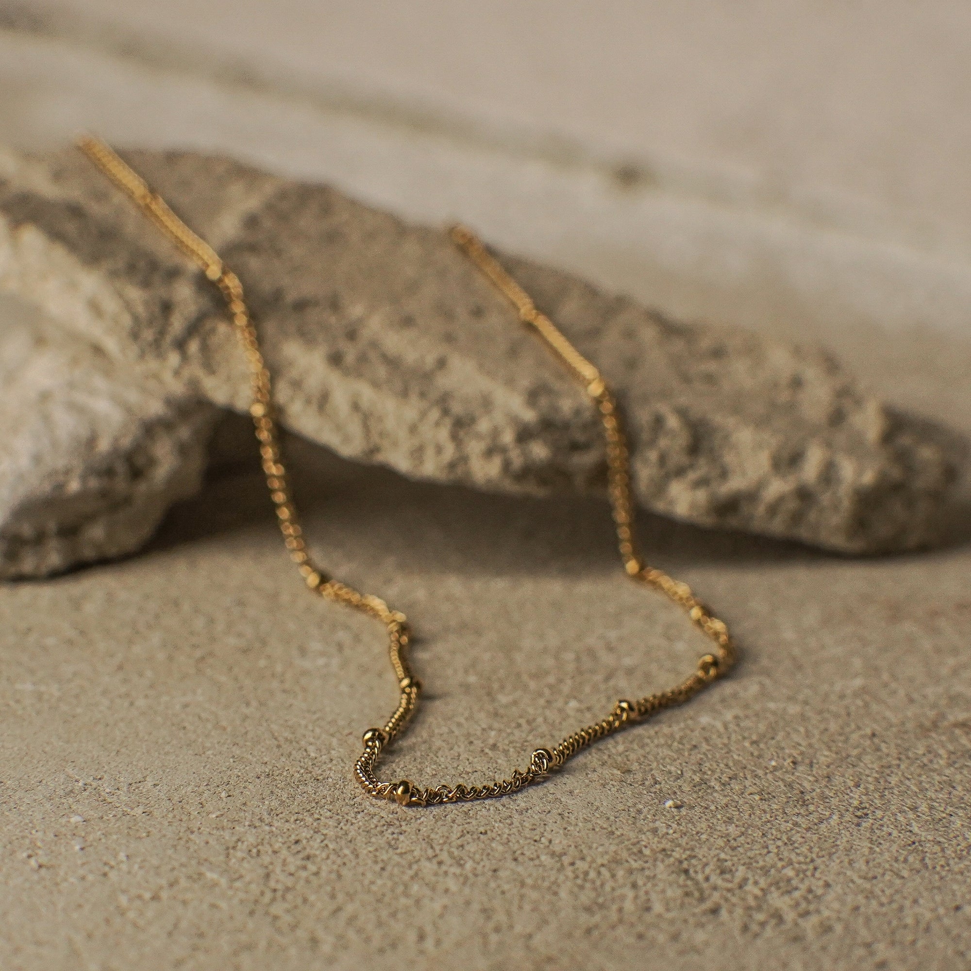 Gold necklace on a sandy surface with rocks in the background