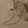 Gold chain necklace on a sandy surface with rocks