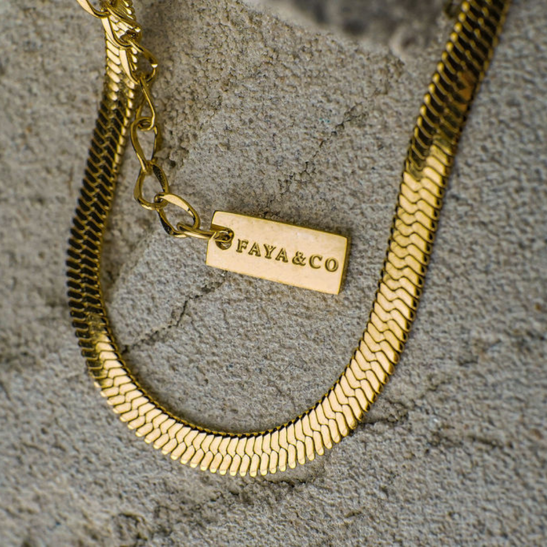 Gold chain bracelet with 'FAYA&CO' tag on a textured surface