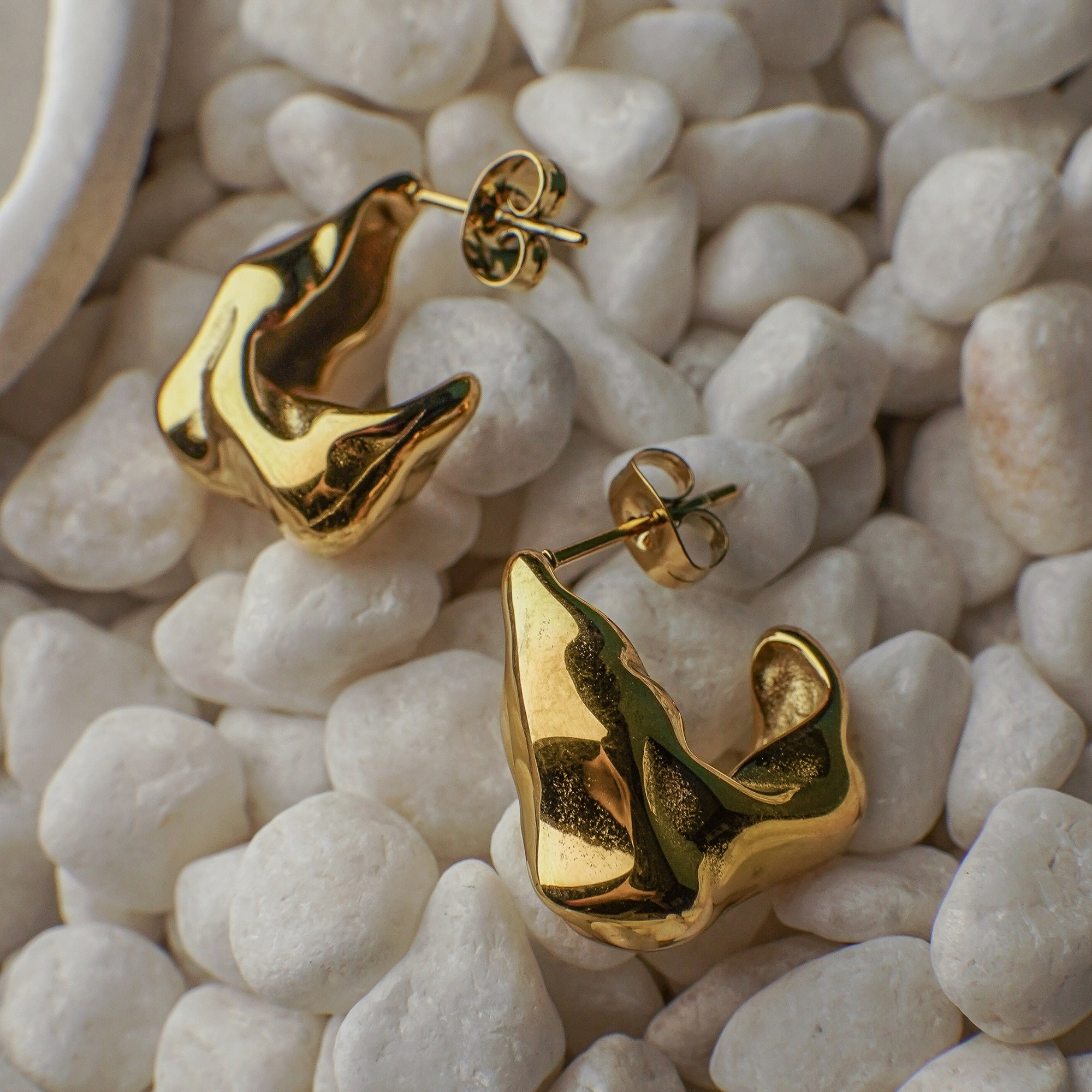 Gold earrings on a textured white stone surface