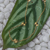Gold necklace with floral pendants on a green leaf with a pebble background