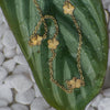 Gold chain necklace with floral pendants on a green leaf
