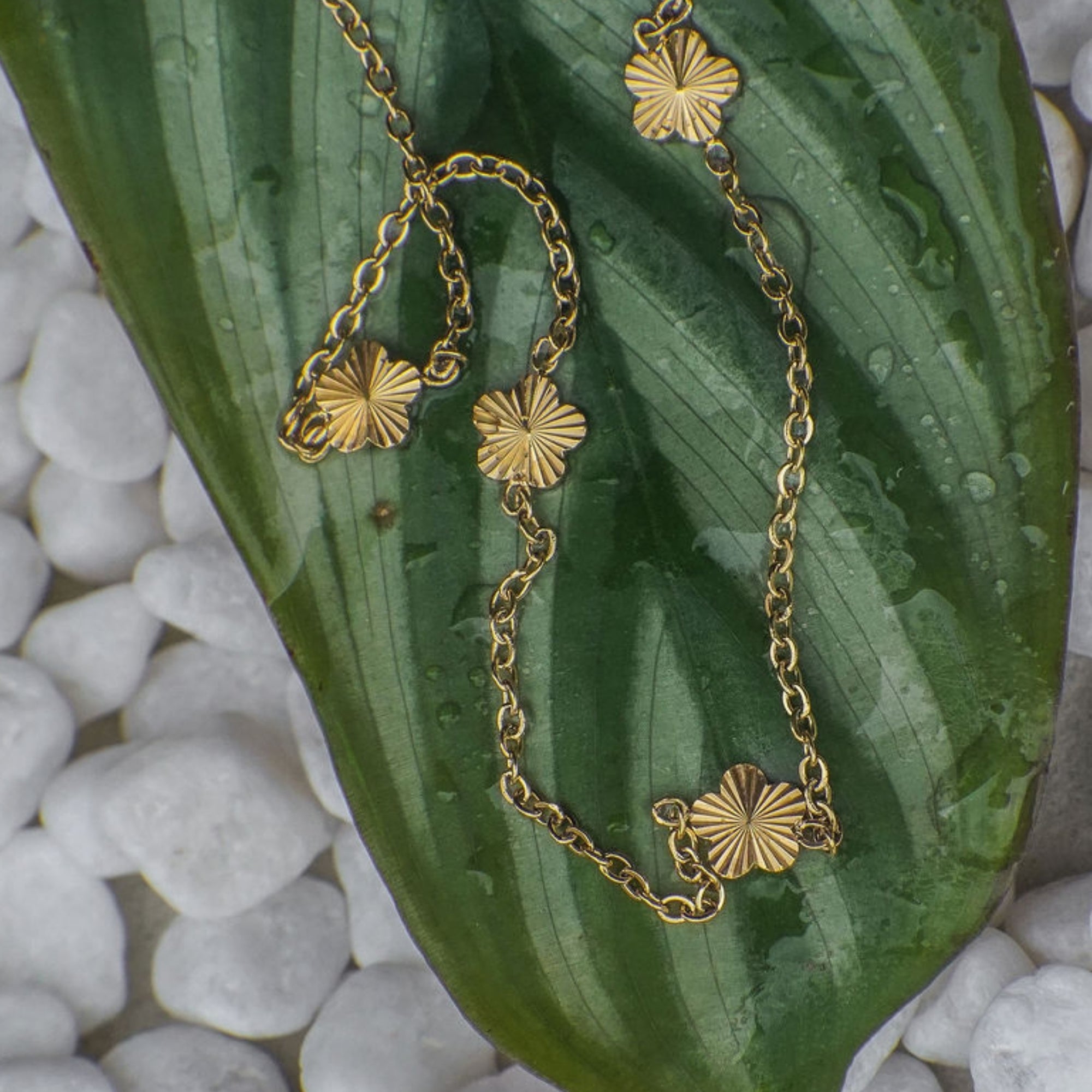 Gold chain necklace with floral pendants on a green leaf