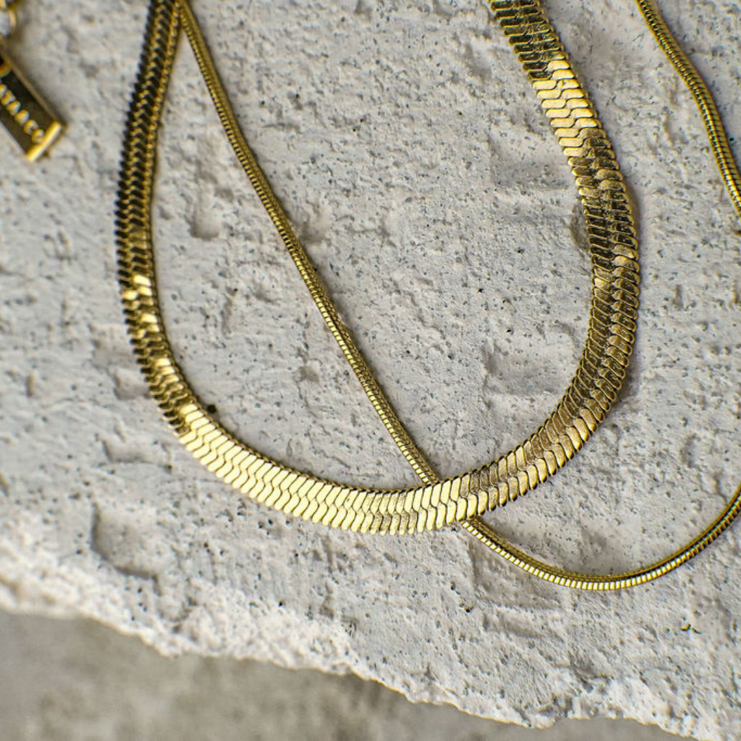 Gold snake chain necklace on a textured stone surface