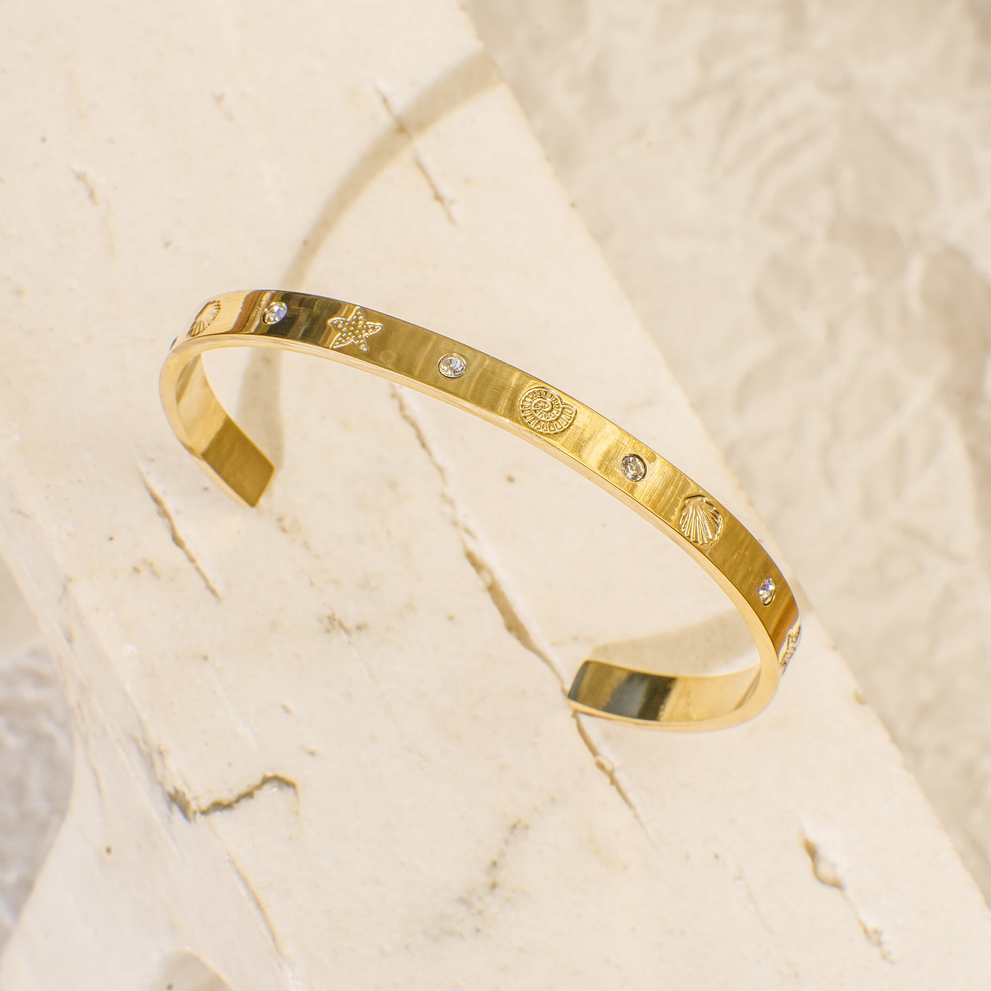 Gold bracelet with engraved design on a beige marble background