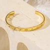 Gold bracelet with engraved designs on a beige surface