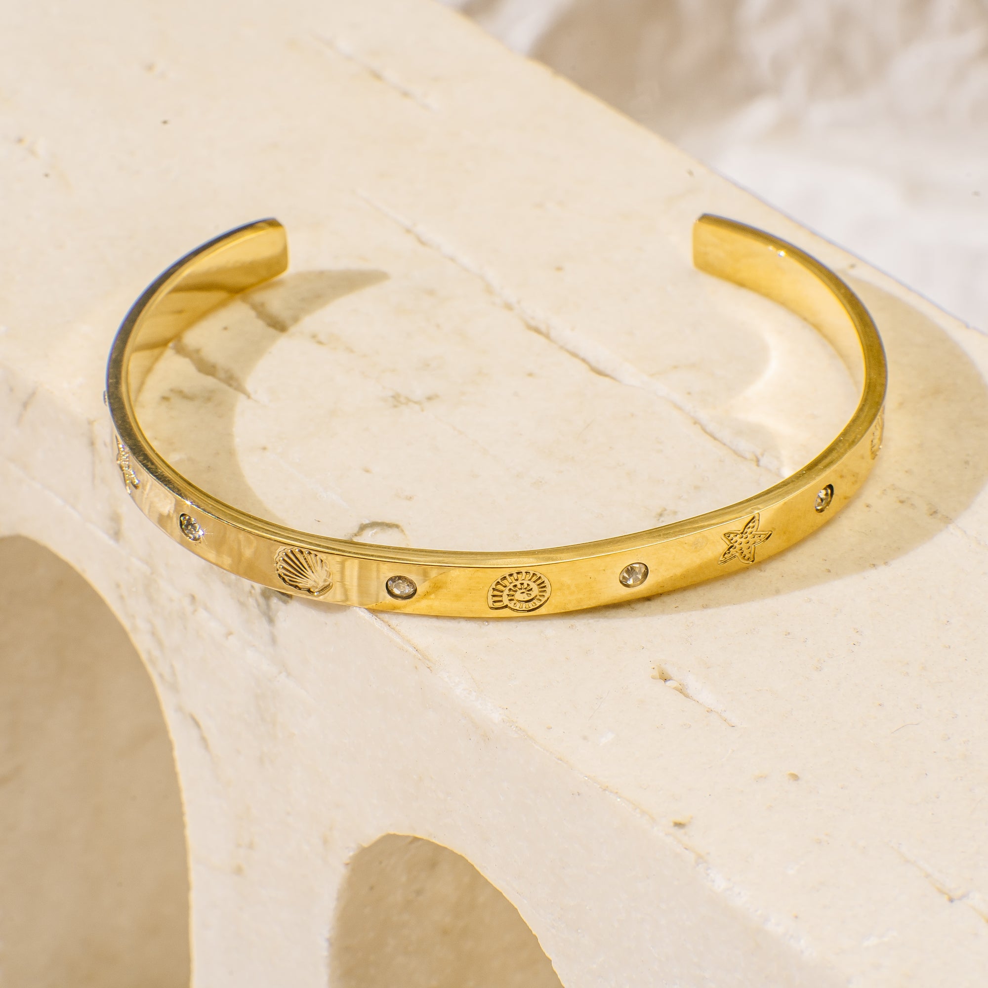 Gold bracelet with engraved designs on a beige surface