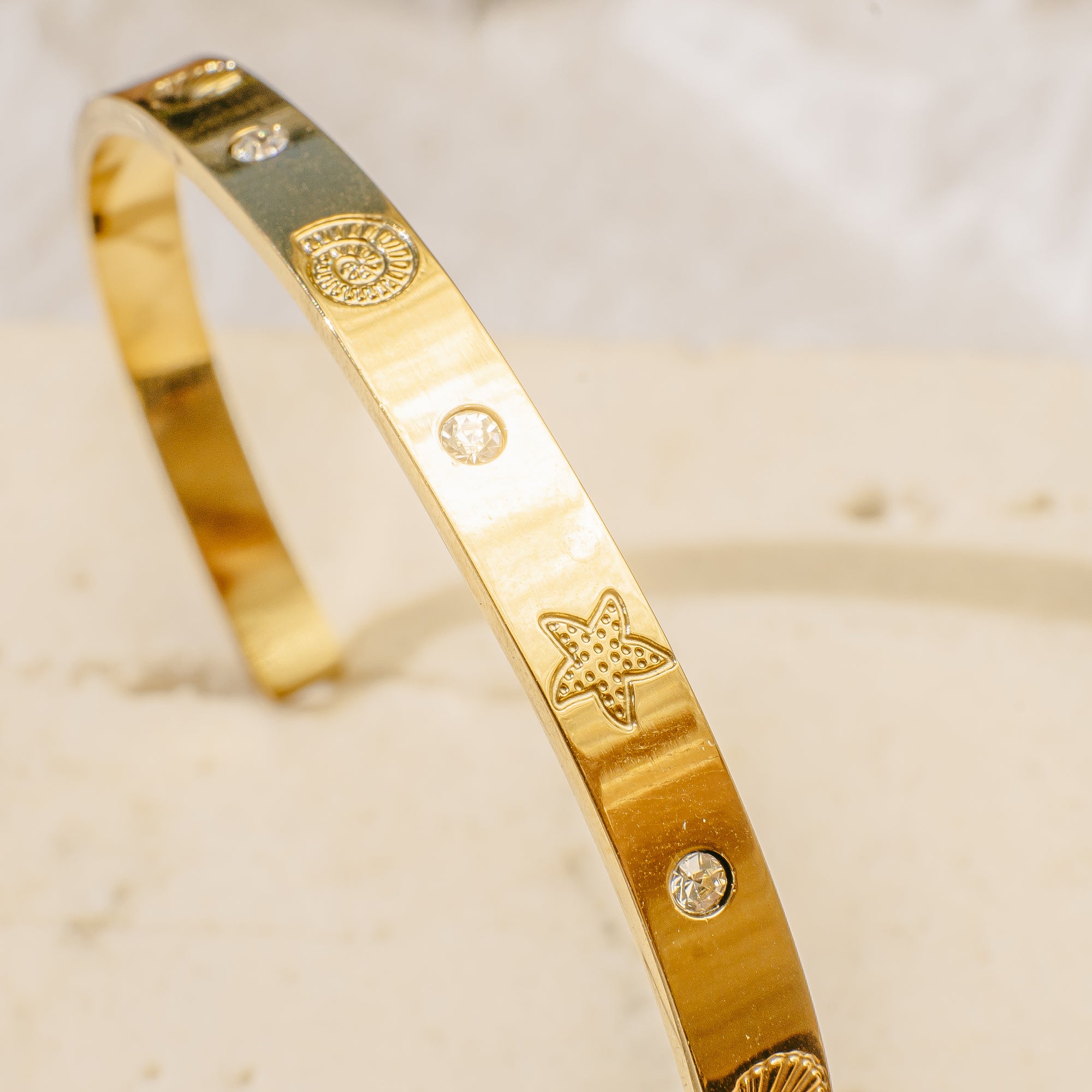 Gold bracelet with star design on a beige surface