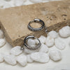Silver hoop earrings with embedded stones on a stone surface