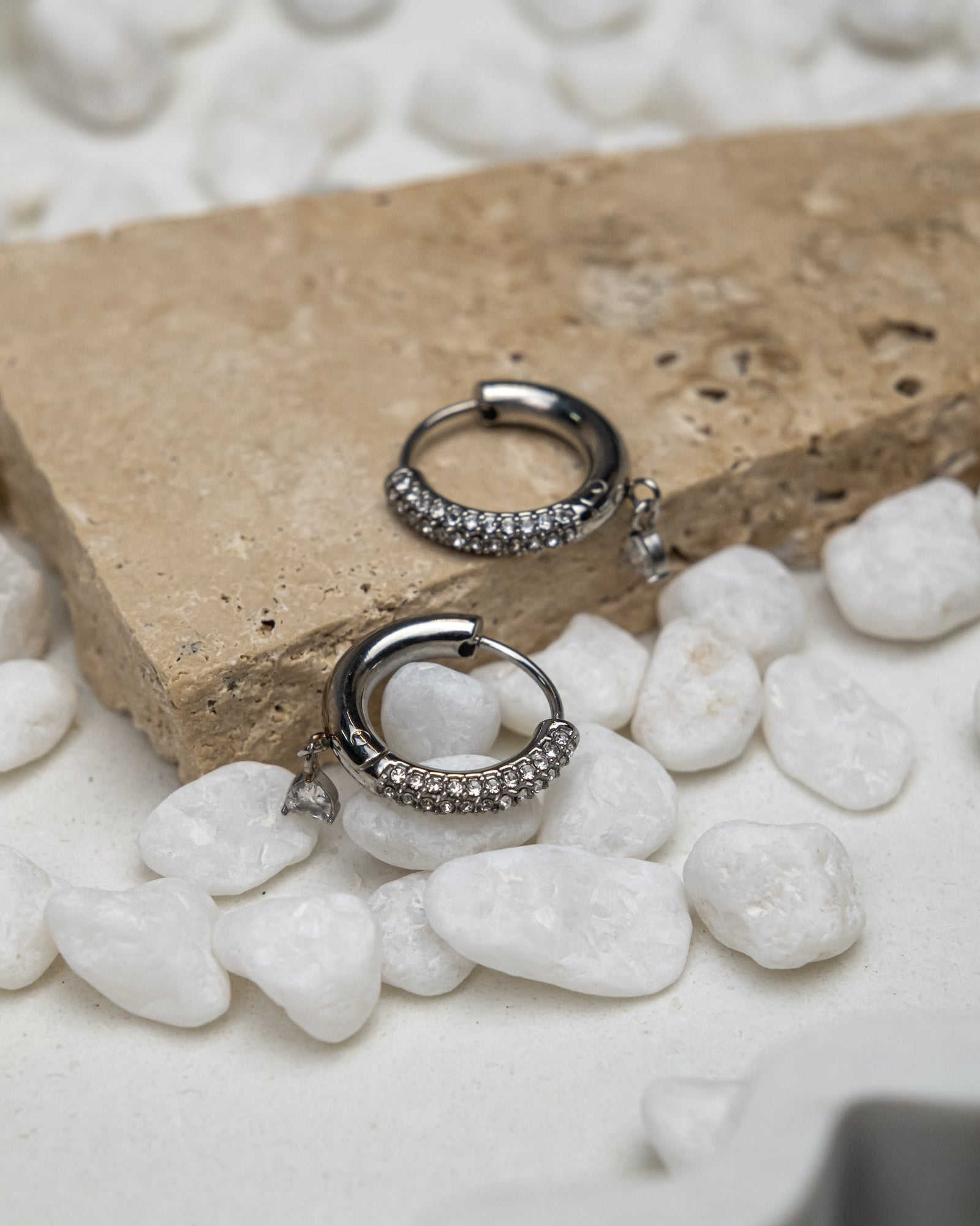 Silver hoop earrings with embedded stones on a stone surface