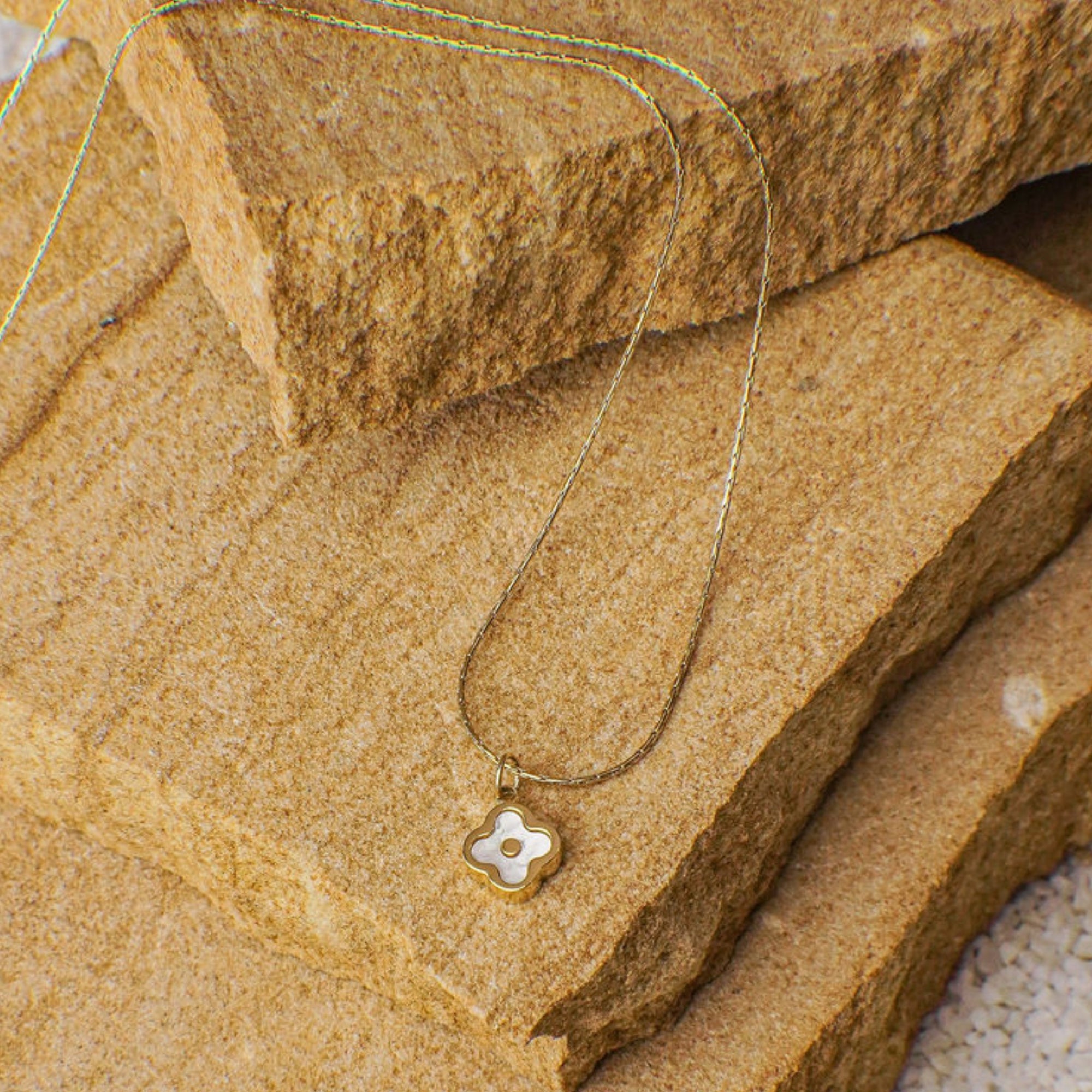 Gold necklace with a floral pendant on a stone surface