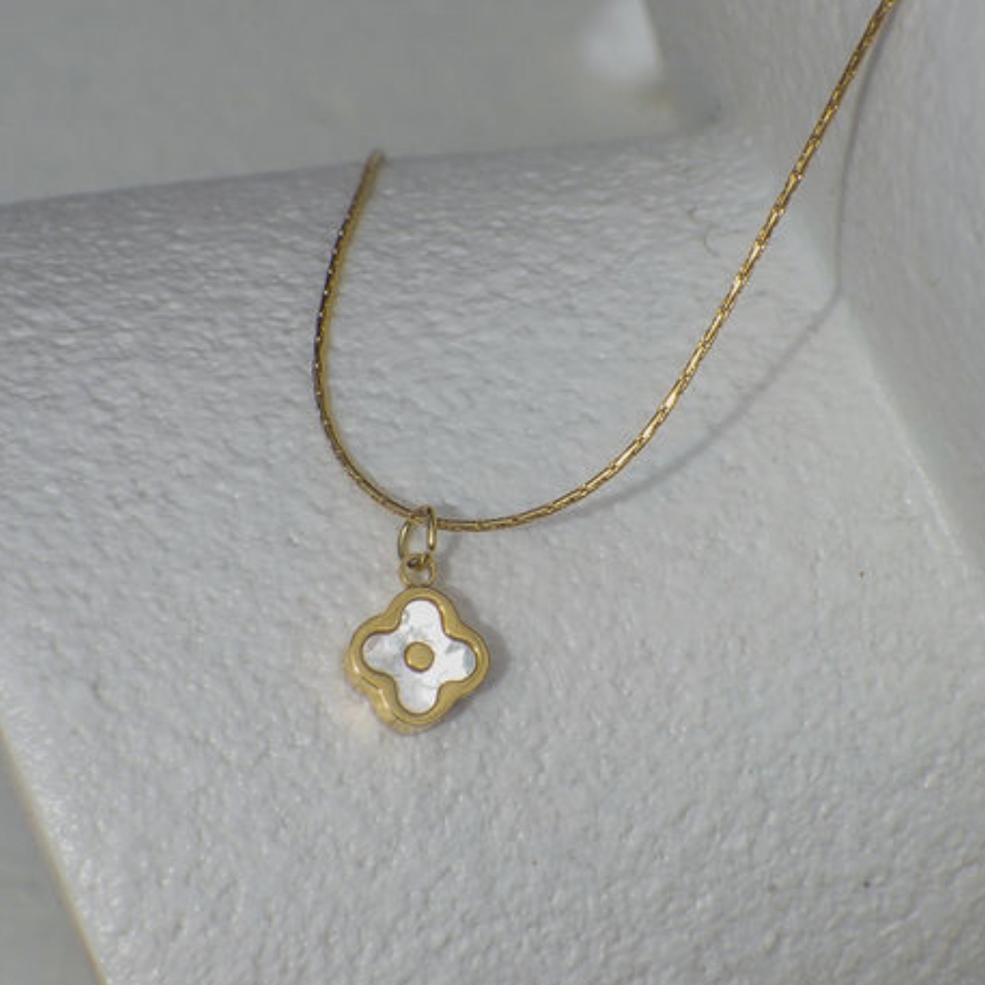 Gold necklace with a clover-shaped pendant on a mannequin bust.