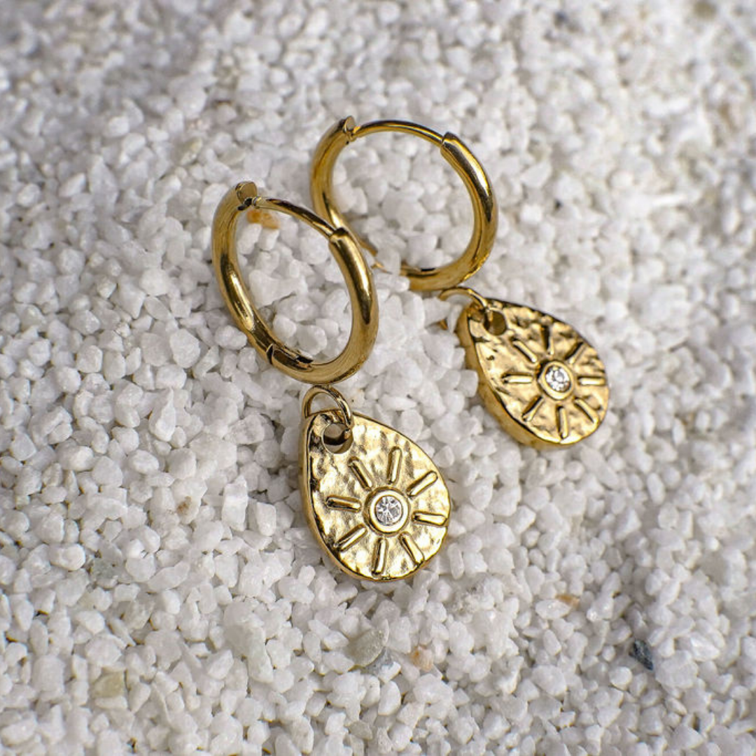 Gold hoop earrings with round pendants on a textured white surface