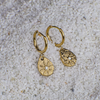 Gold hoop earrings with teardrop-shaped charms on a textured white surface