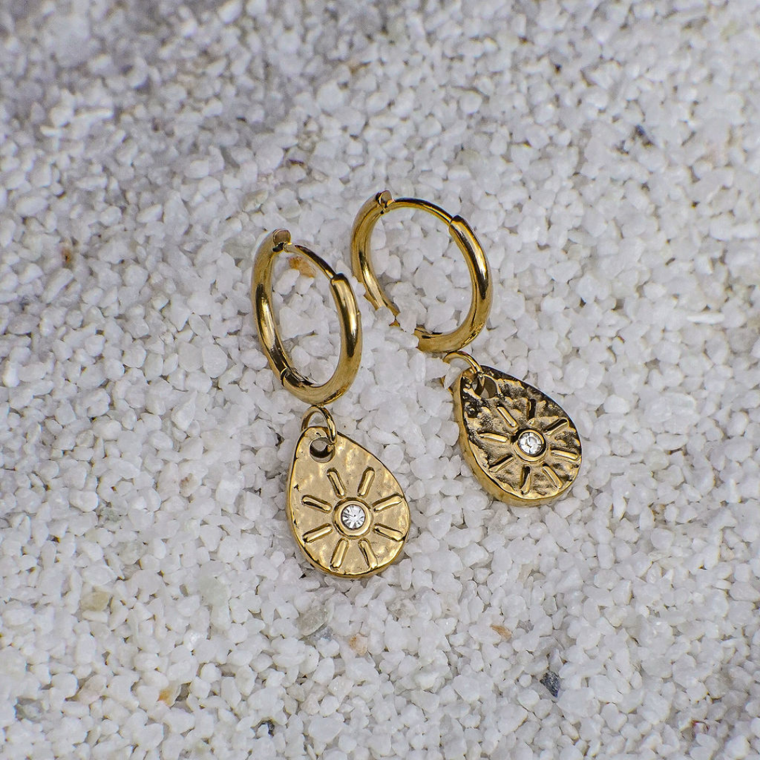 Gold hoop earrings with teardrop-shaped charms on a textured white surface