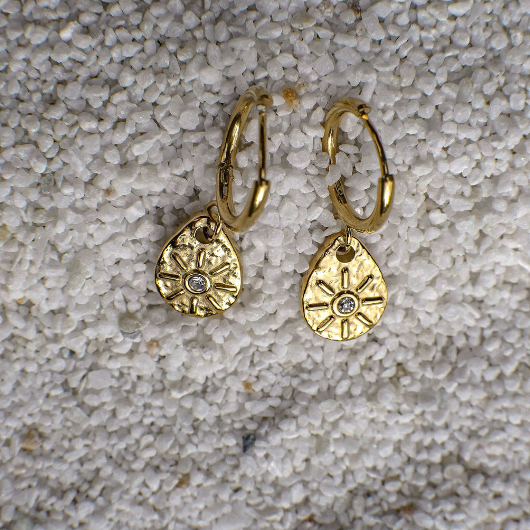Gold hoop earrings with textured designs on a textured surface