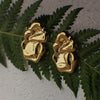 Gold earrings on green leaves against a gray background