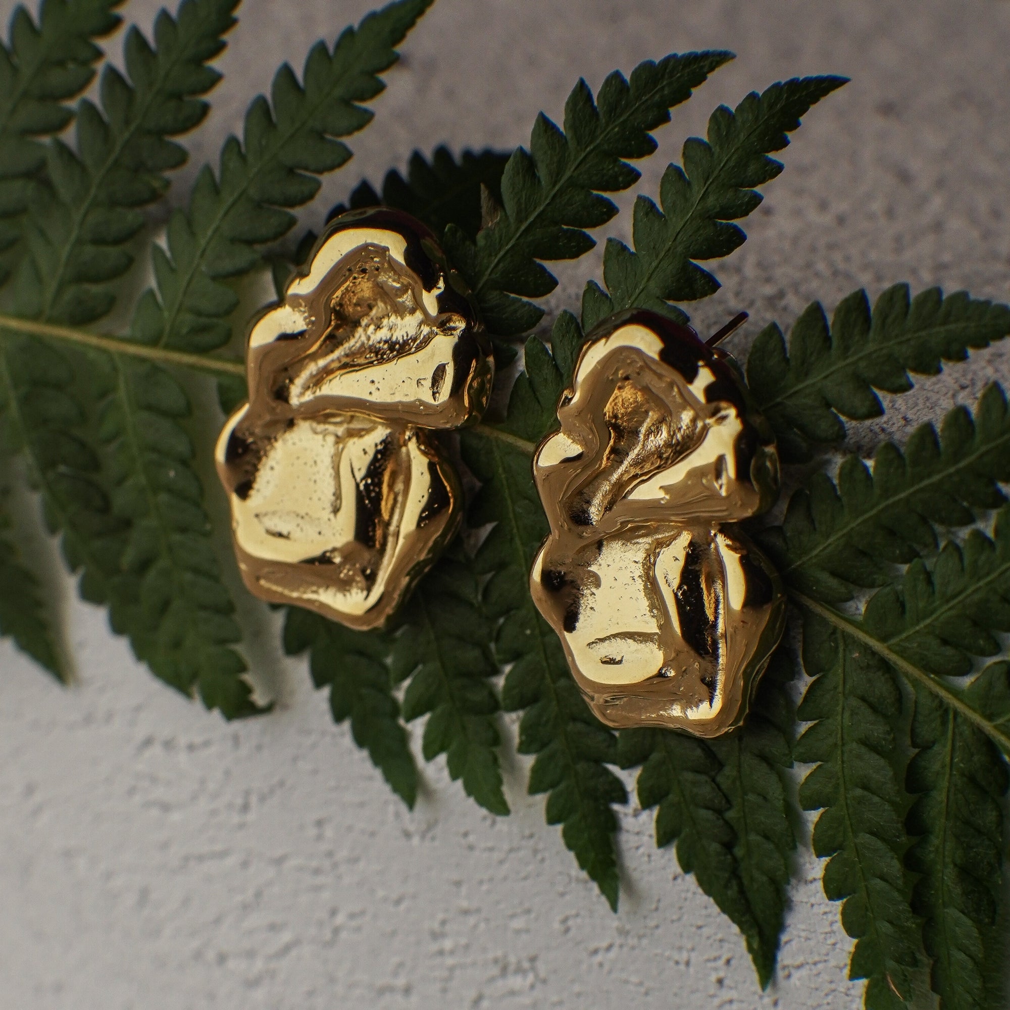 Gold earrings on green leaves against a gray background