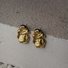 Gold bee-shaped earrings on a textured surface
