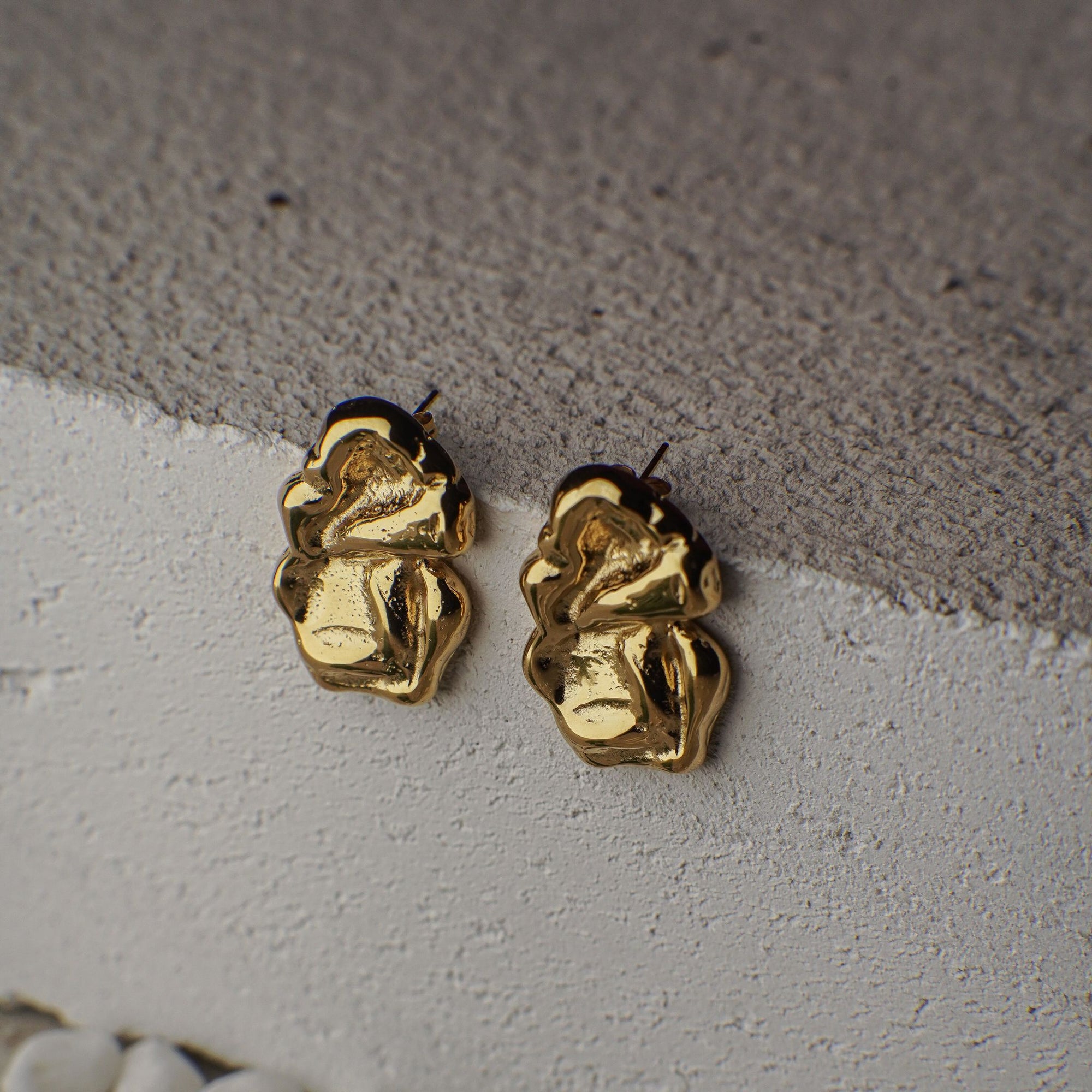 Gold bee-shaped earrings on a textured surface