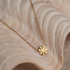 A gold-colored necklace with a round pendant featuring a geometric design, displayed on a textured background.