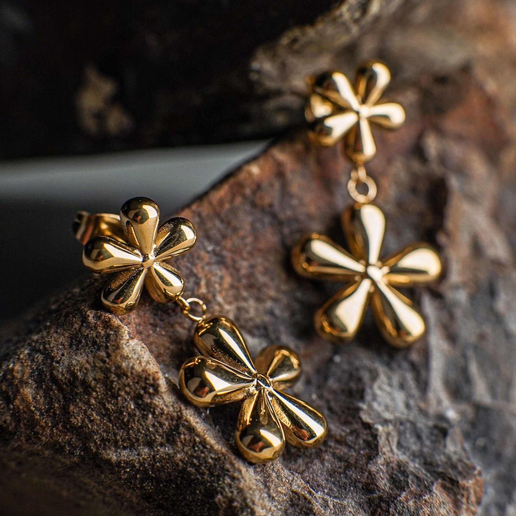 Gold four-leaf clover earrings on a textured stone surface