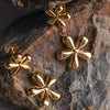 Gold four-leaf clover earrings on a textured stone surface