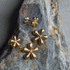 Gold flower-shaped earrings on a textured stone surface