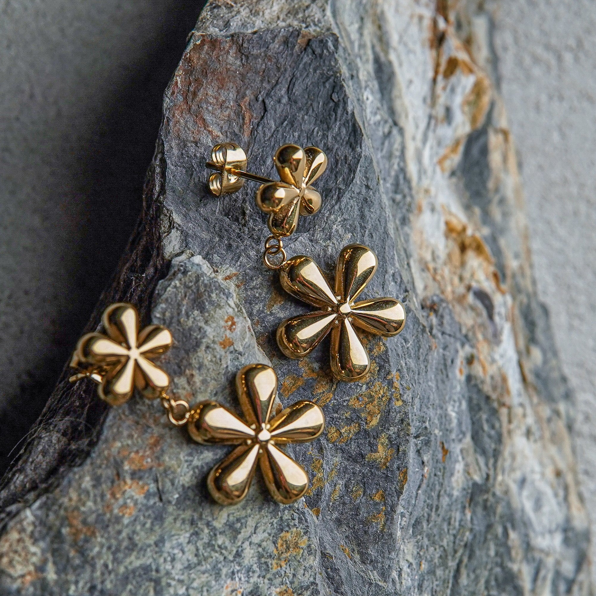 Gold flower-shaped earrings on a textured stone surface