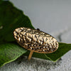 Gold textured ring on a green leaf with a gray background