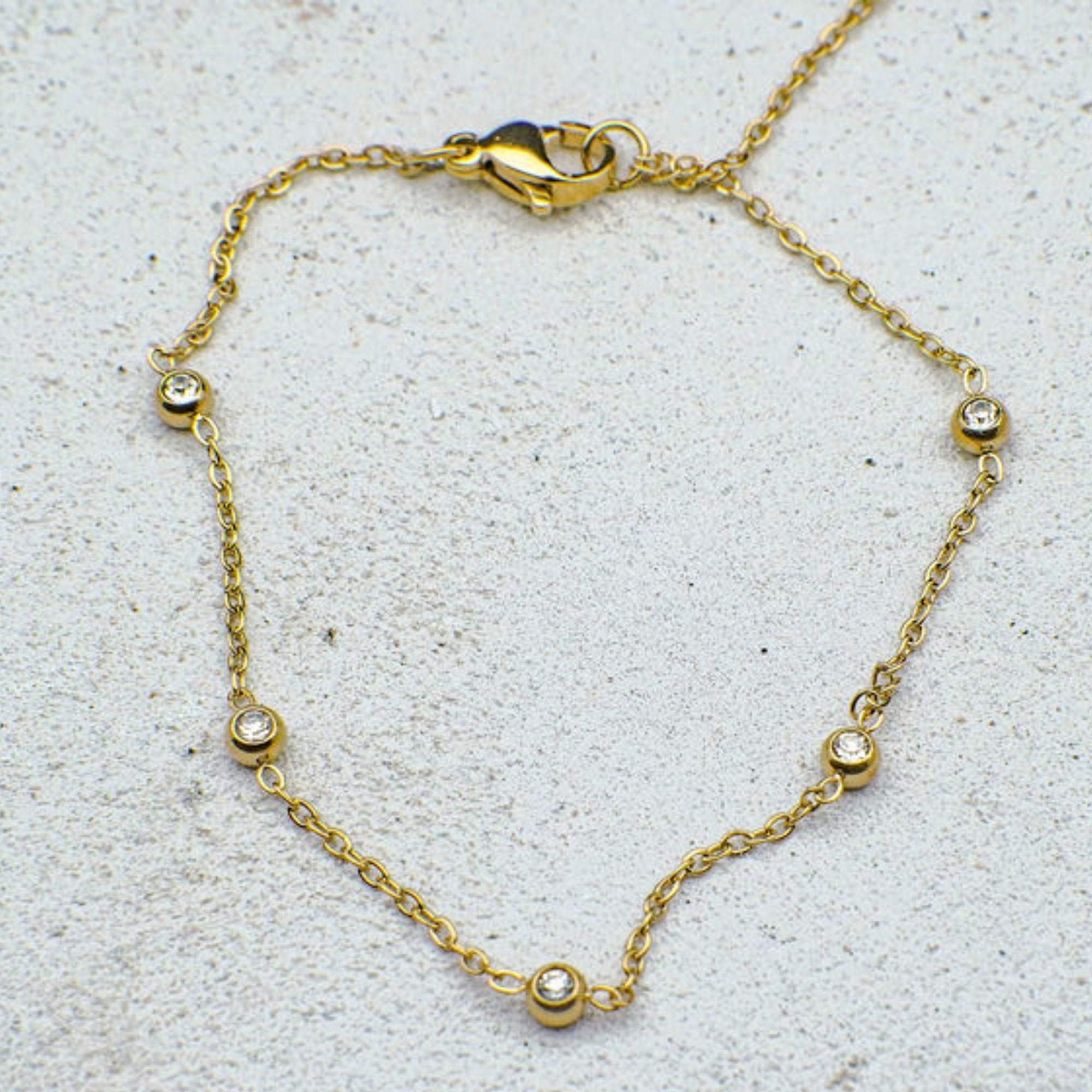 Gold bracelet with small gemstones on a light gray background