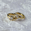 Gold ring with two square-cut diamonds on a textured white background