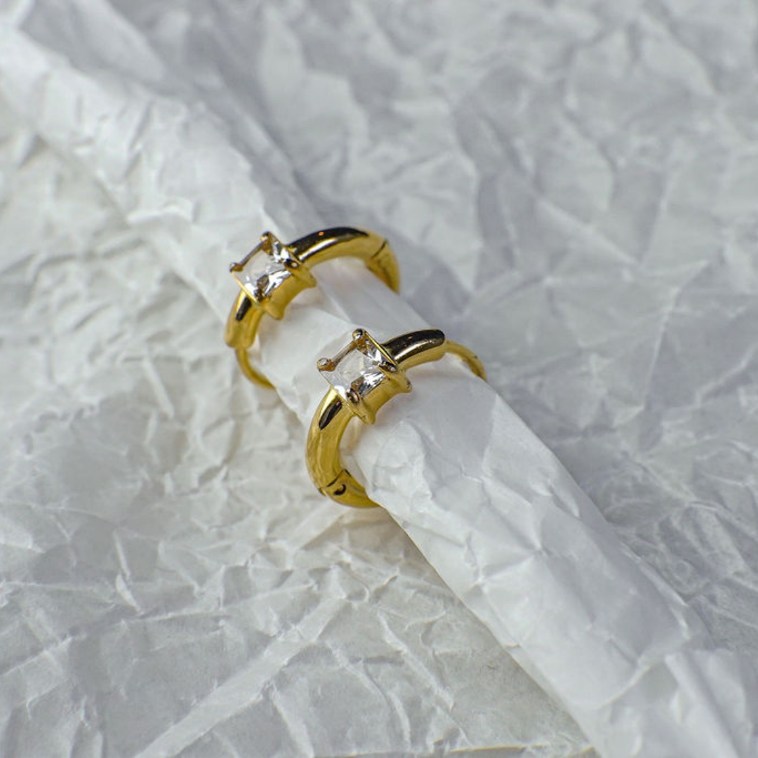 Gold hoop earrings with clear gemstones on a textured white fabric background