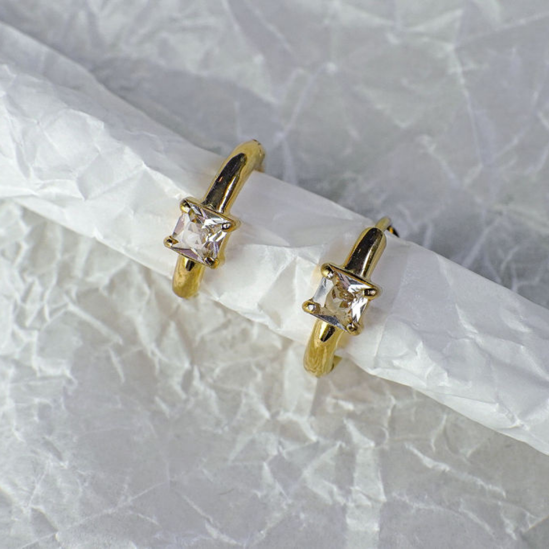 Gold hoop earrings with clear gemstones on a textured white background