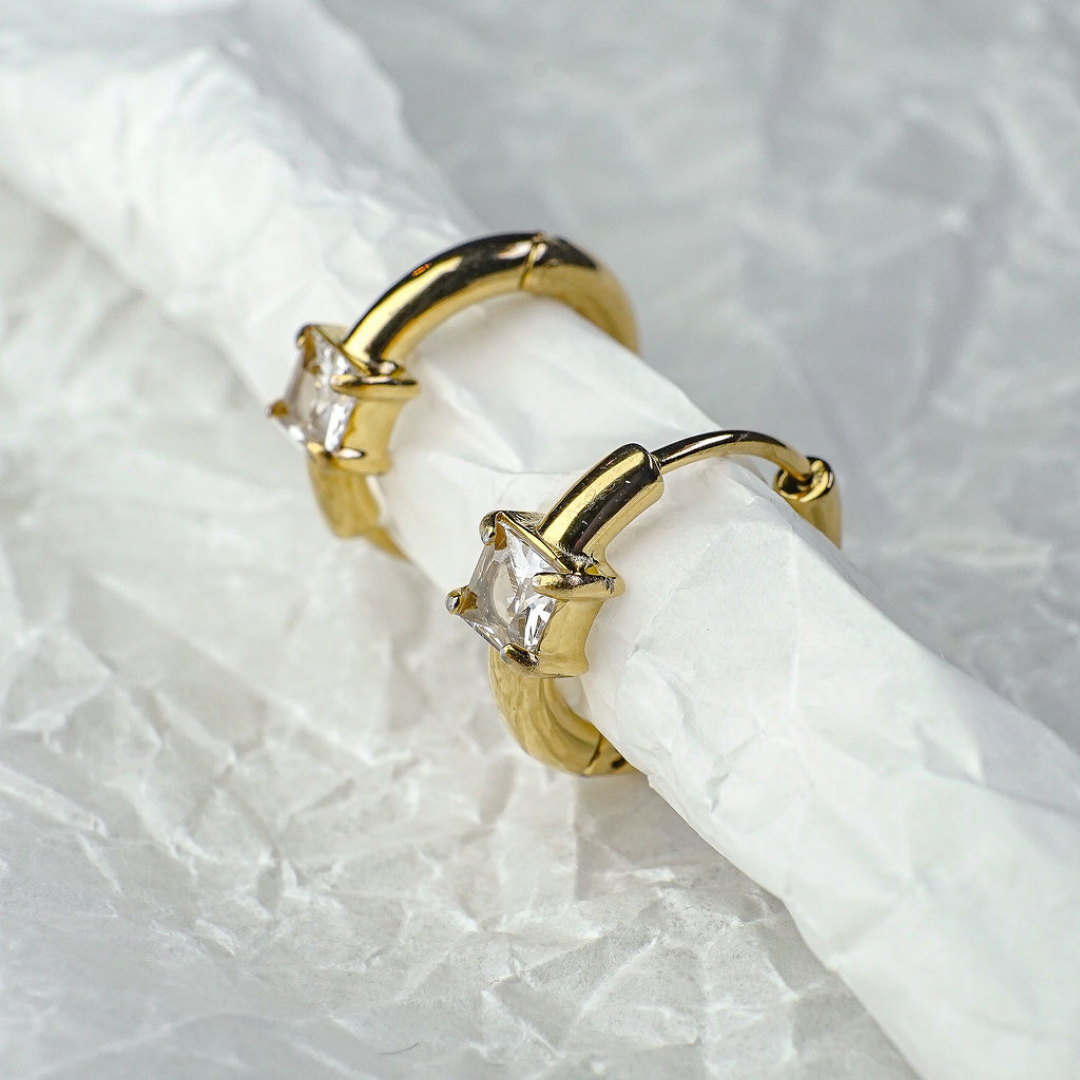 Gold hoop earrings with clear gemstones on a white fabric background