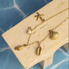 Gold necklace with shell and starfish pendants on a beige stand against a blue textured background