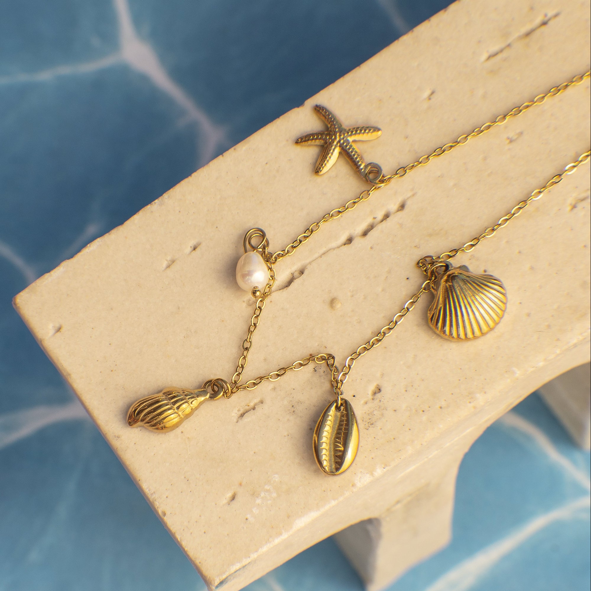 Gold necklace with shell and starfish pendants on a beige stand against a blue textured background