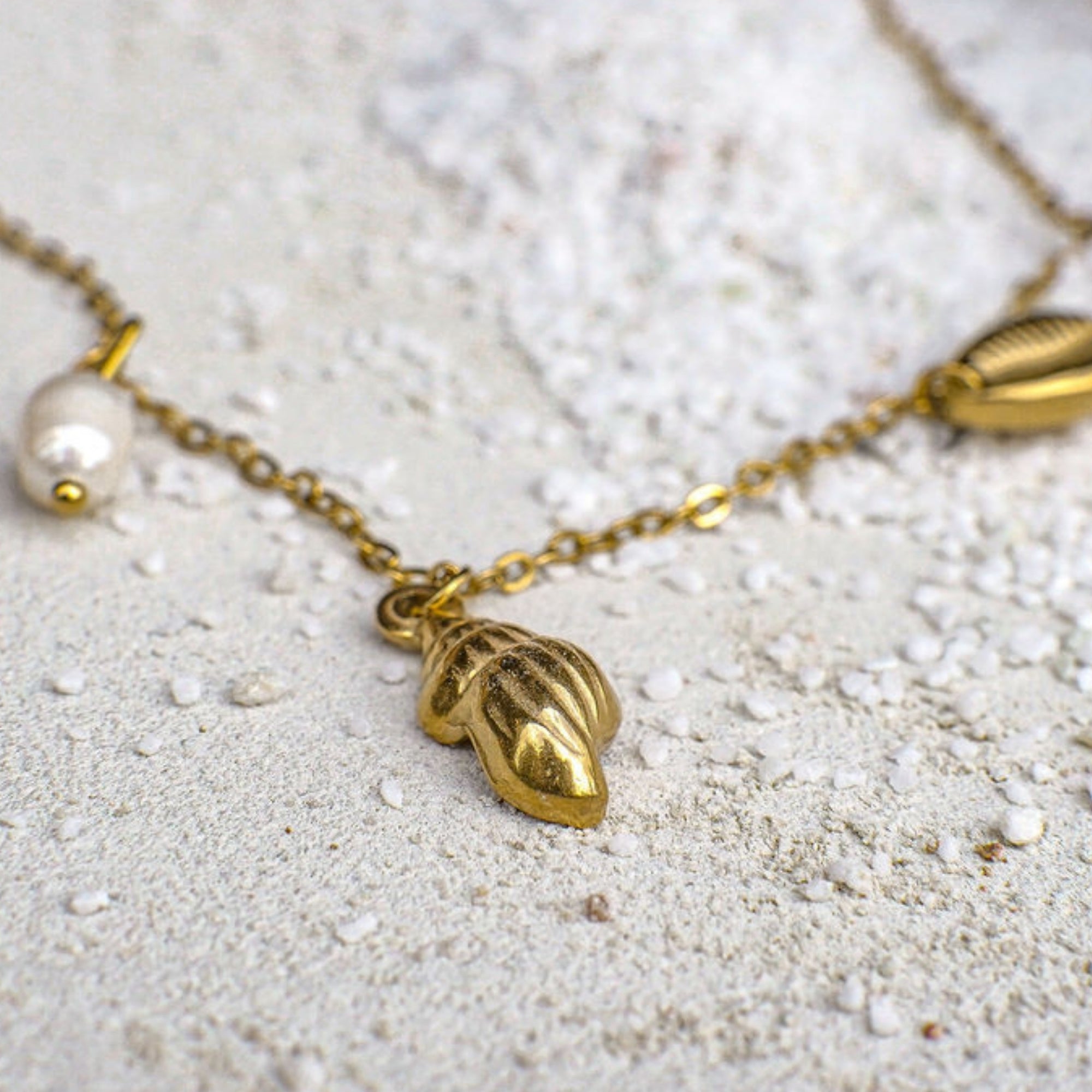 Gold necklace with leaf-shaped pendant and pearl on a light background