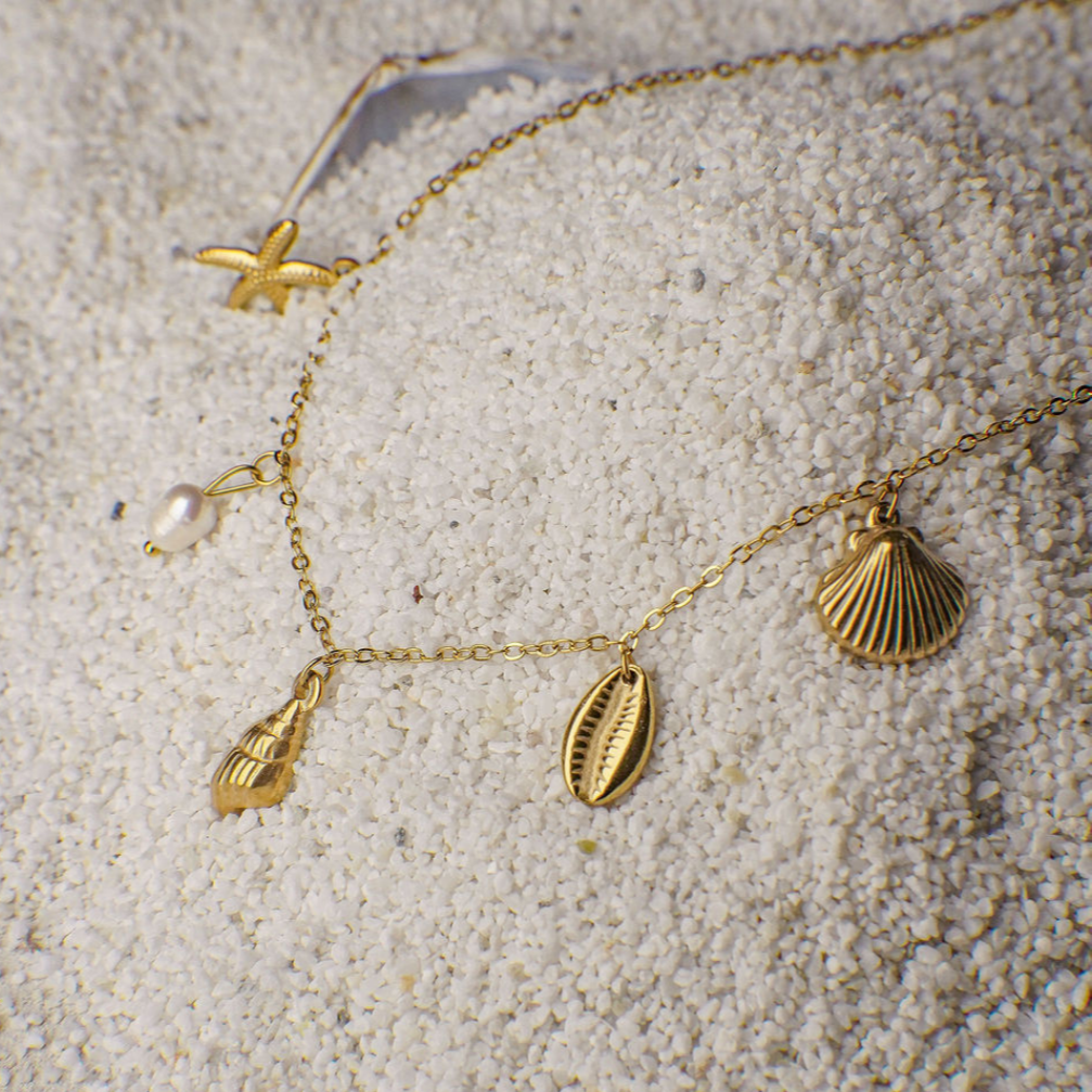 Gold necklace with shell-shaped charms on a sandy surface