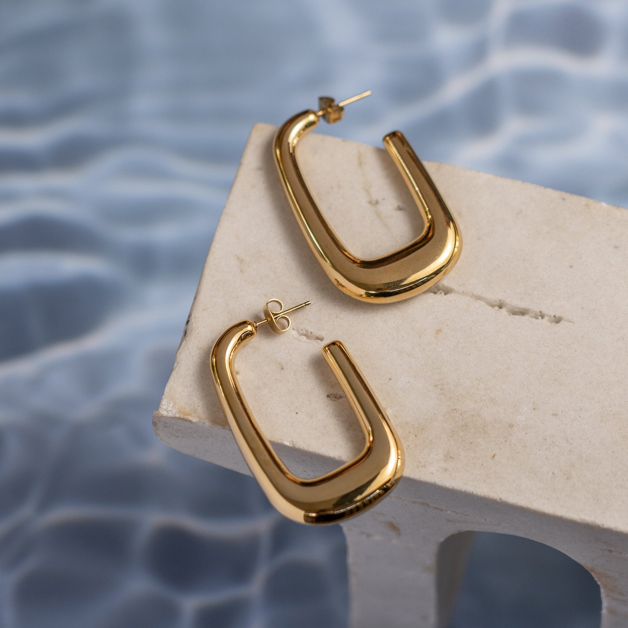 A pair of shiny gold u-shaped hoop earrings on a textured wood