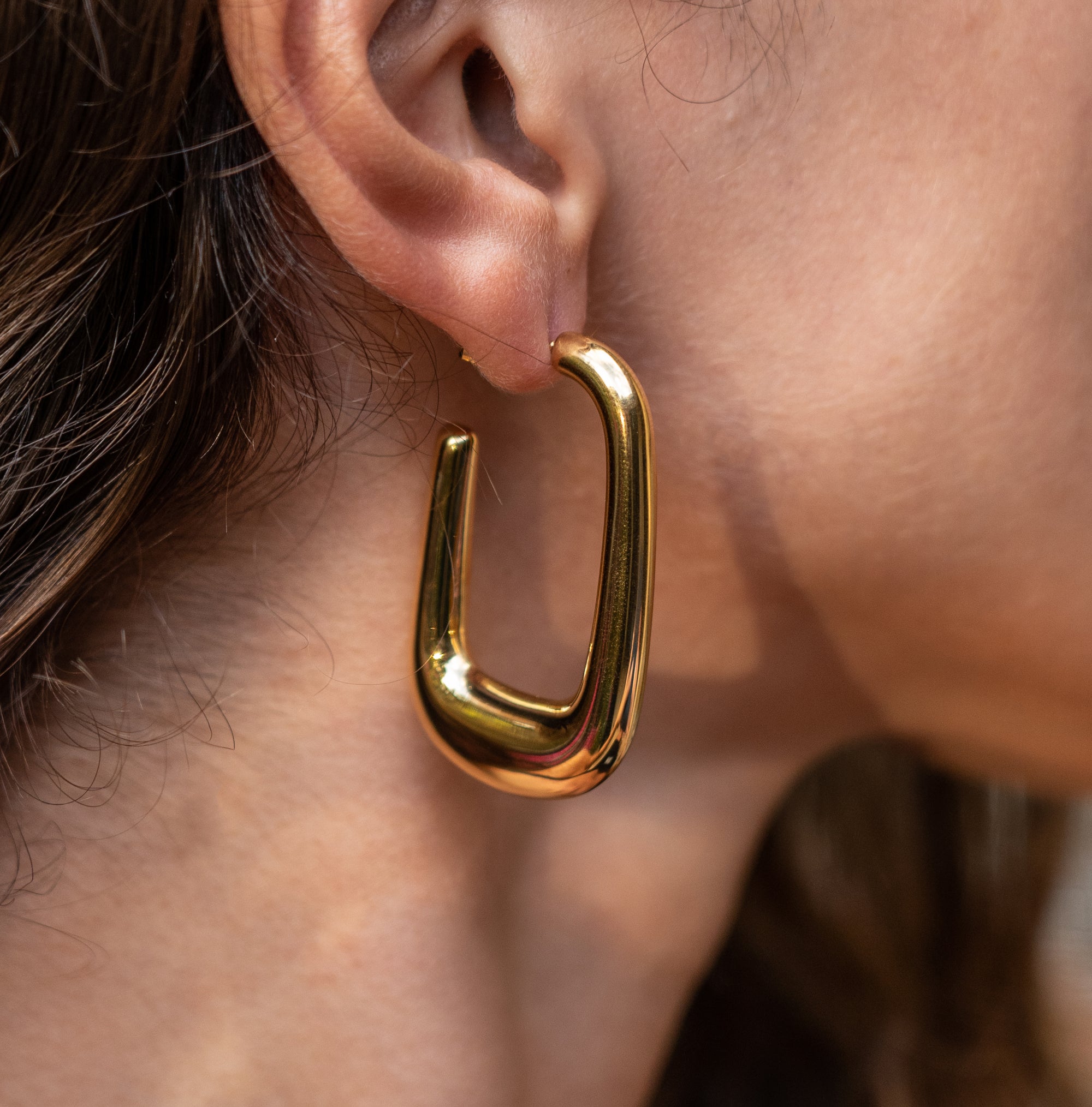 A shiny gold u-shaped hoop earrings on a model's ear