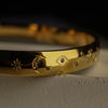 Gold bracelet with star and circle designs on a dark background