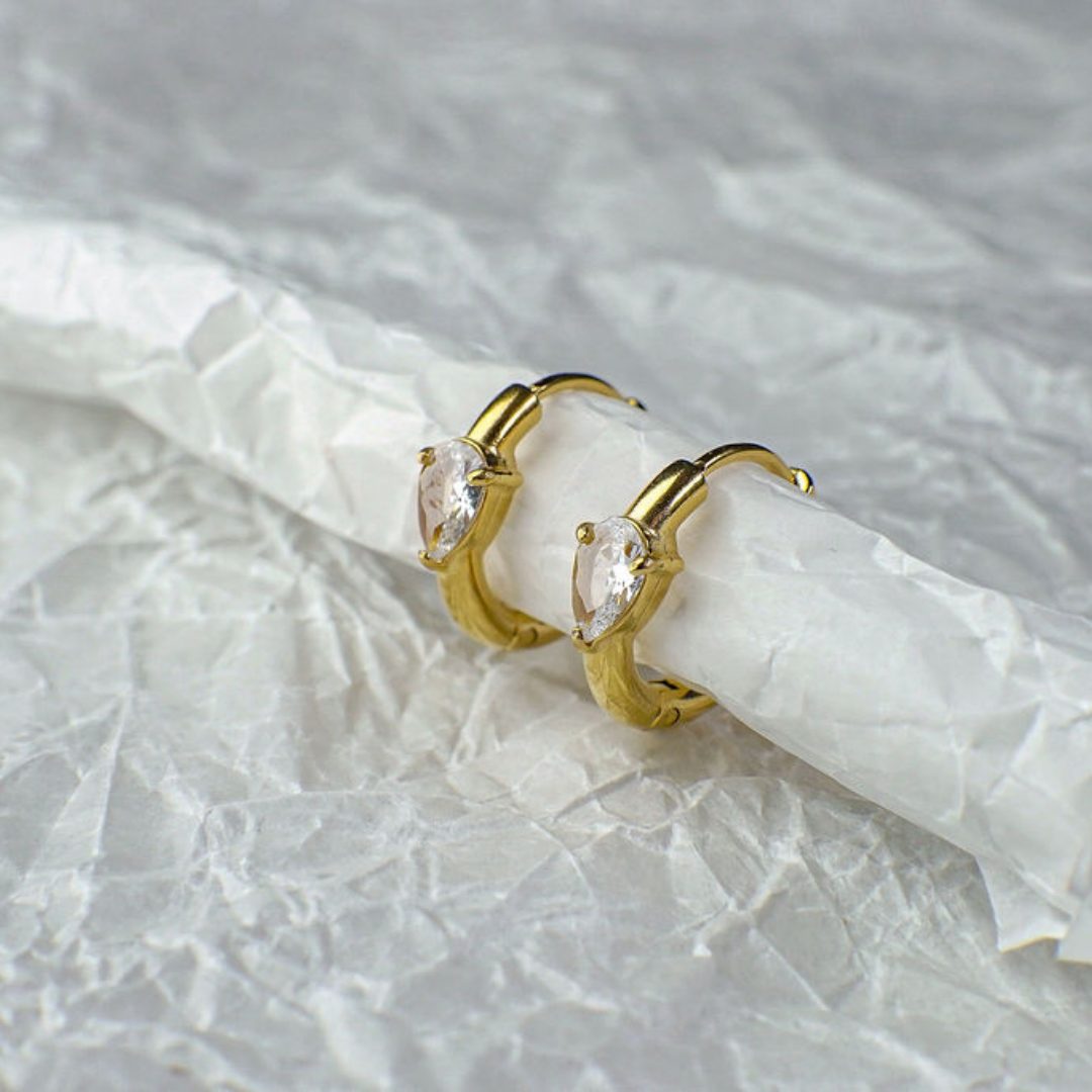 Gold hoop earrings with clear gemstones on a textured white background