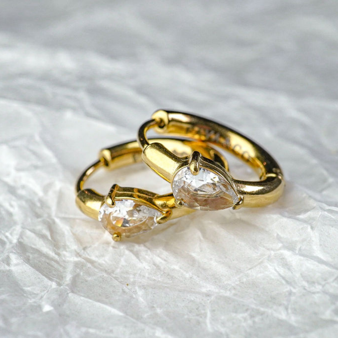 Two gold hoop earrings with clear gemstones on a textured white background