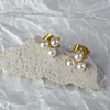 Gold and pearl stud earrings on a textured white surface