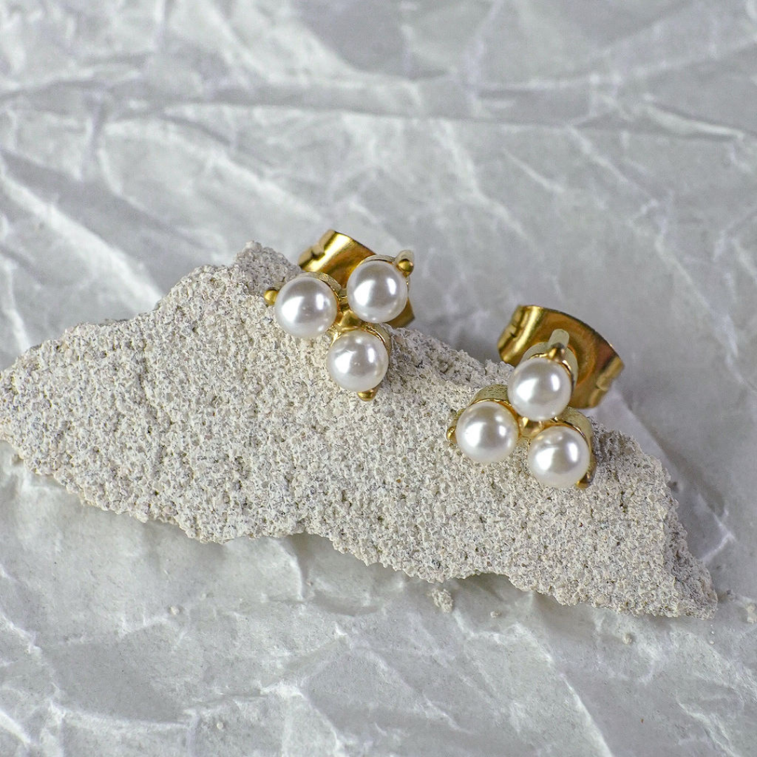 Gold and pearl stud earrings on a textured white surface