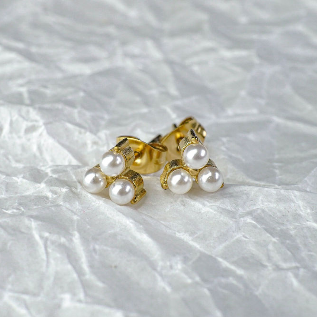 Gold earrings with pearls on a textured white background