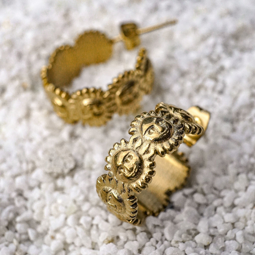 Gold hoop earrings with intricate designs on a textured white surface